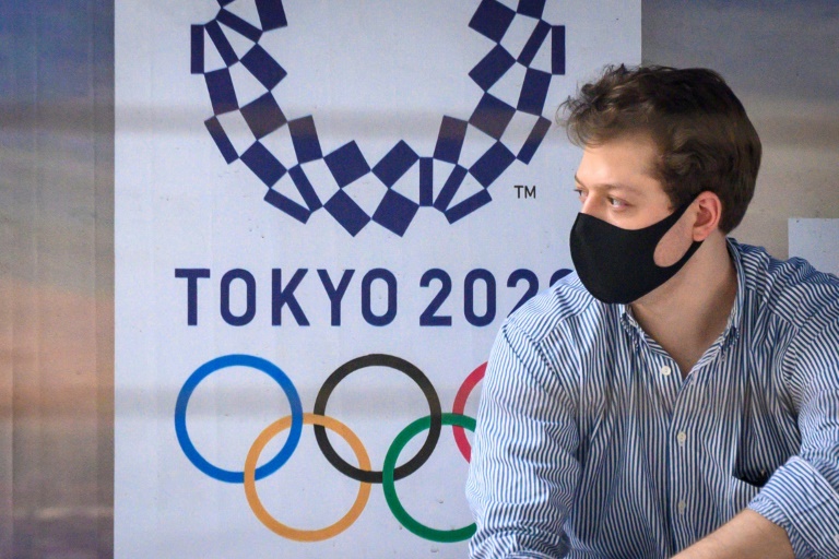 Un hombre con mascarilla protectora aguarda en una parada de autobús que expone un cartel de los Juegos Olímpicos de Tokio, el 16 de marzo de 2020 en Bangkok, la capital tailandesa.