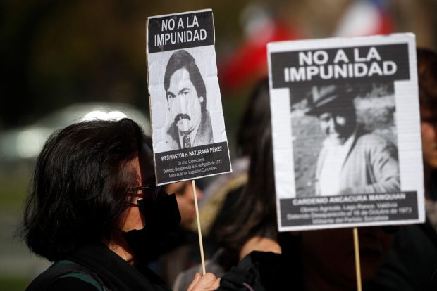 Personas sosteniendo carteles con los rostros de detenidas y detenidos desaparecidos en Chile.