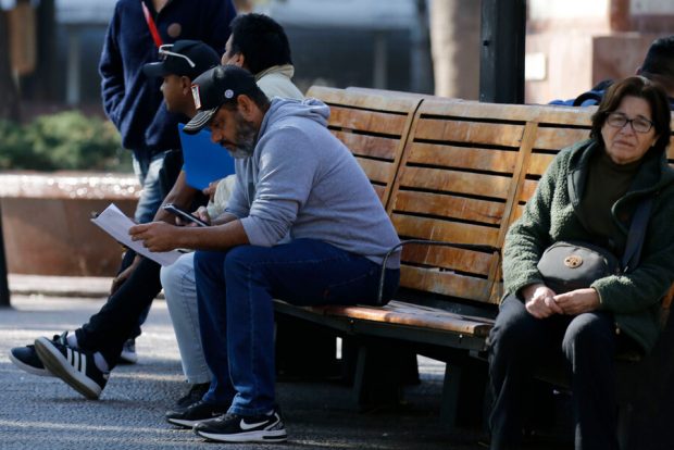 hombre mira papeles y su celular en una banca