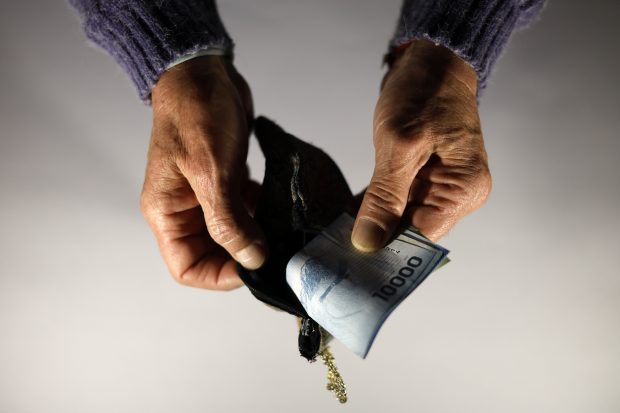 Manos de persona mayor sacando billetes de una billetera.