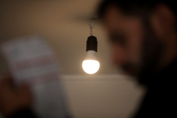 Bombilla encendida colgando del techo, con un fondo borroso que incluye la silueta de una persona sosteniendo lo que parece ser una factura