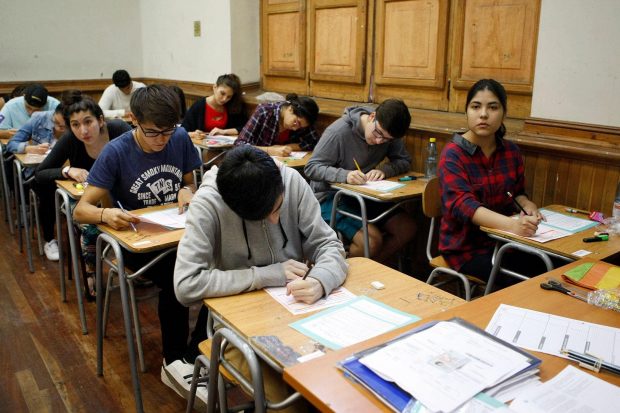 Dos filas de pupitres con estudiantes rindiendo una prueba escrita.