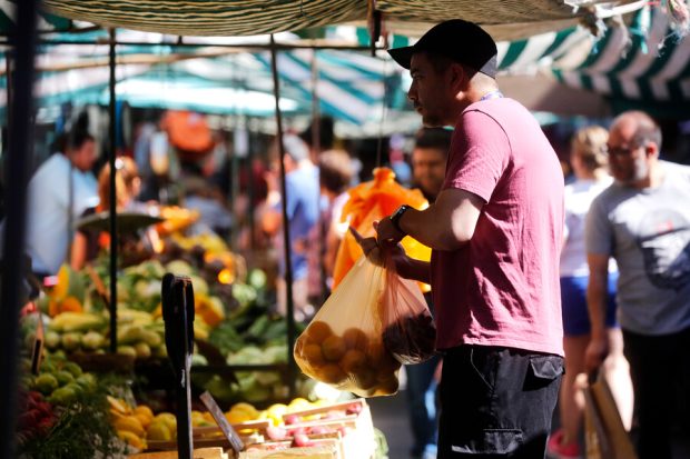 Sujeto con bolsa de verduras en su mano mientras compra otros alimentos en la feria.