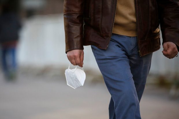 Hombre camina con mascarilla blanca en la mano.