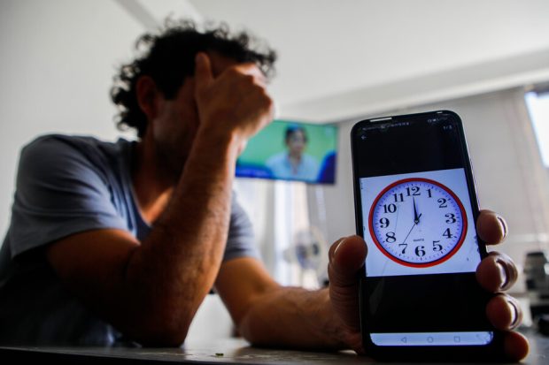 Hombre se tapa el rostro con frustración mientras muestra un teléfono que indica el cambio de hora.