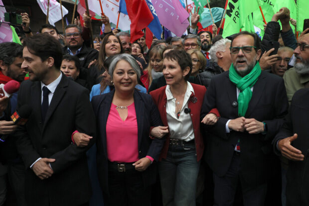 Los candidatos presidenciales del oficialismo (de izquierda a derecha): Gonzalo Winter (FA), Jeannette Jara (PC), Carolina Tohá (PPD) y Jaime Mulet (FRVS). Detrás de ellos una multitud de personas con banderines de distintos colores.