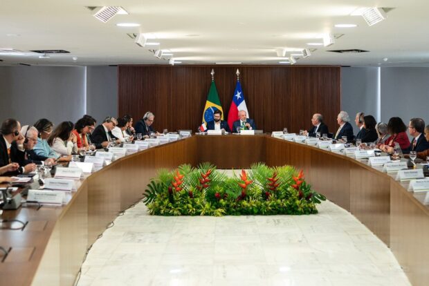 Presidente Boric y Lula encabezan reunión de mesa tipo herradura, detrás de ellos la bandera de Chile y Brasil.