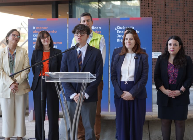 Estudiante secundario da testimonio en el lanzamiento de la Encuesta de Juventud y Bienestar 2024, acompañado por autoridades como Natalia Riffo (SENDA), Emilia Ríos (Deporte), Carolina Leitao (Prevención del Delito) y representantes del Gobierno, en el Centro Cultural GAM.