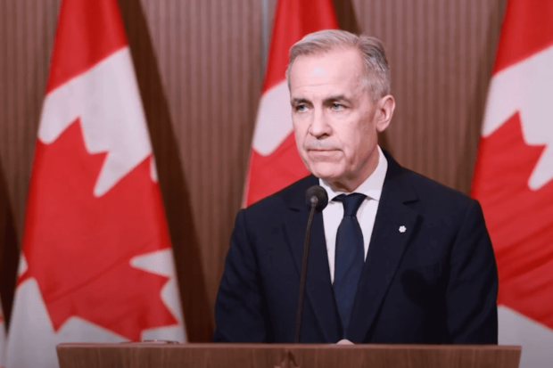 Primer ministro de Canadá, Mark Carney, frente a un podio, atrás de él tres banderas de Canadá.