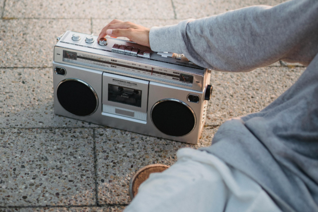 En la imagen se ve una radio en el suelo y una persona sentada al lado mientras toca sus botones
