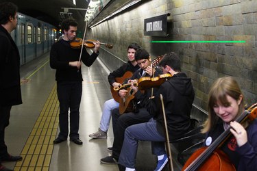 Músicos jóvenes tocando violines, guitarra y chelo en el andén de una estación de metro, junto a un tren detenido