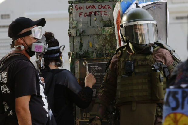 Manifestantes con mascarillas antigases frente a un carabinero con equipo antidisturbios durante el estallido social en Chile.