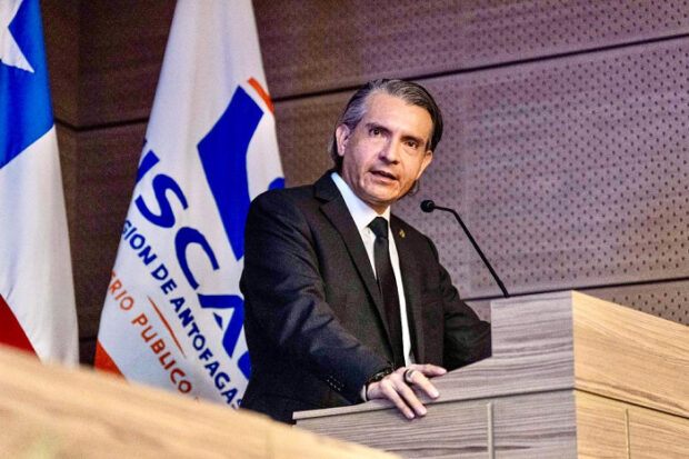 Juan Castro Bekios, fiscal regional de Antofagasta, hablando delante de un podio. Detrás de él una bandera blanca con el logo de la Fiscalía.