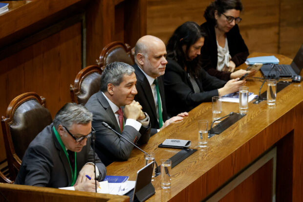Tres hombres (Cox, Duran y Elizalde) sentados en sitiales mirando a un público que no se ve. A su lado dos mujeres, Aisen Etcheverry y Macarena Lobos) revisando unos documentos. Un mesa de madera brillosa esa frente a ellos.