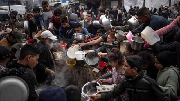 Niños gazatíes aglomerados con ollas en las manos a la espera de recibir algo de comida.