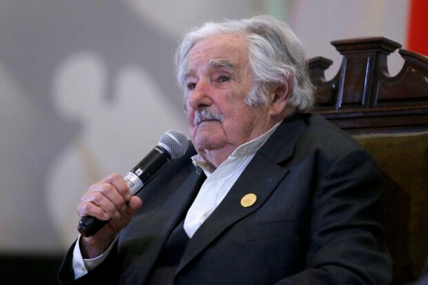 Pepe Mujica sentado en un sitial café con un micrófono en la mano.