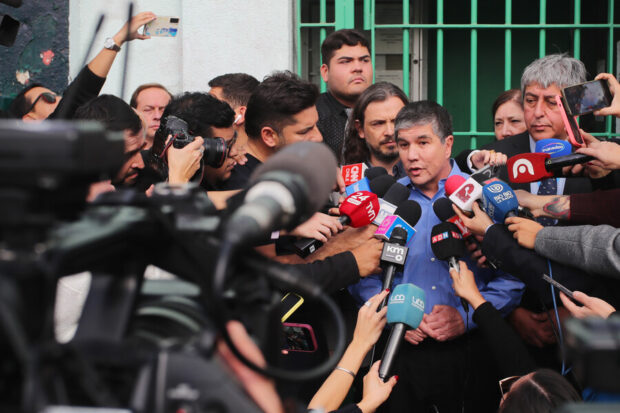 Manuel Monsalve rodeado de periodistas y camarógrafos mientras responde preguntas ante los micrófonos de distintos medios de comunicación.