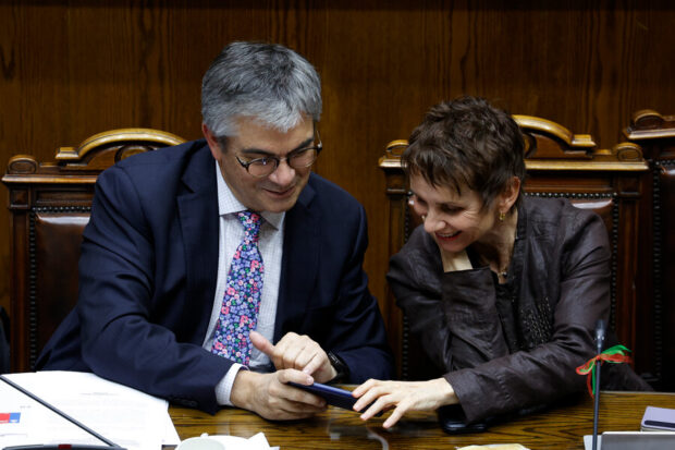 Carolina Tohá y Mario Marcel revisando el celular de Marcel mientras sonríen.