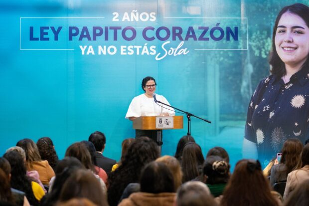 Ministra Antonia Orellana en un podio frente a un público. Detrás de ella una gigantografía que dice: 2 años Ley Papito Corazón, ya no estás sola.