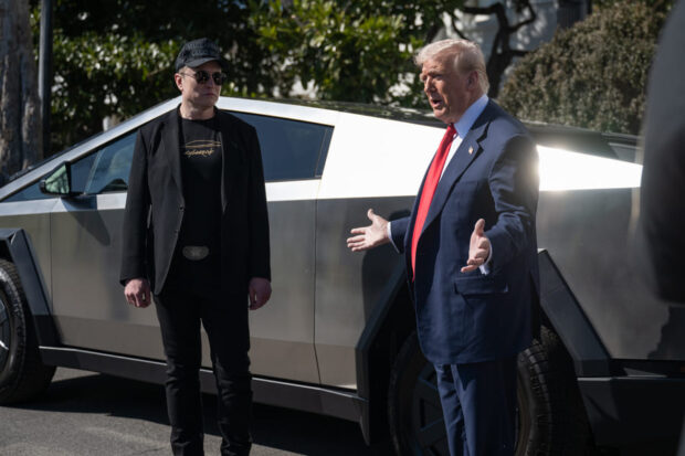 Donald Trump y Elon Musk conversando, detrás de ellos un telsa, un auto plateado.