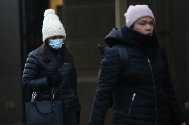 Dos mujeres abrigadas caminando en la calle, una además de su ropa invernal usa mascarilla.