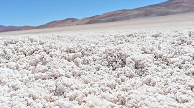 Primer plano de un yacimiento de litio en una salina de alta montaña, con montañas al fondo bajo un cielo despejado.