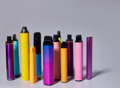 Varios cigarrillos electrónicos o vapeadores de colores brillantes alineados sobre una superficie gris.