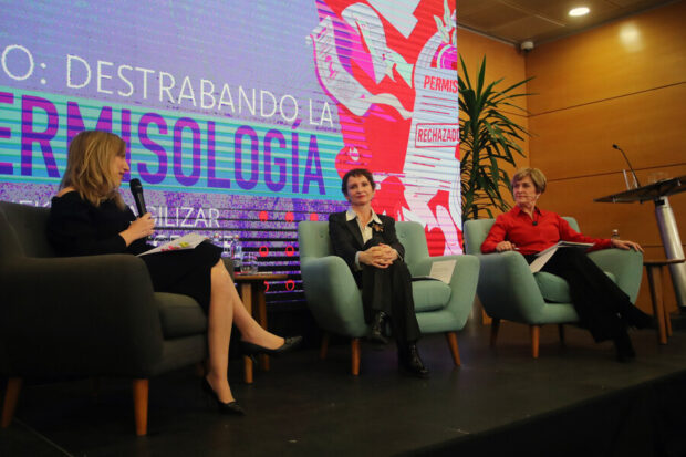 Tres mujeres sentadas en sillones individuales en una pequeña tarima. De izquierda a derecha se ve a moderada, Carolina Tohá y Evelyn Matthei.