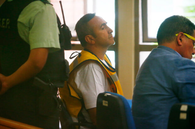 Francisco Pulgar vestido de chaquelo amarillo y polera blanco, a su lado su abogado defensor y detrás de él un carabinero.