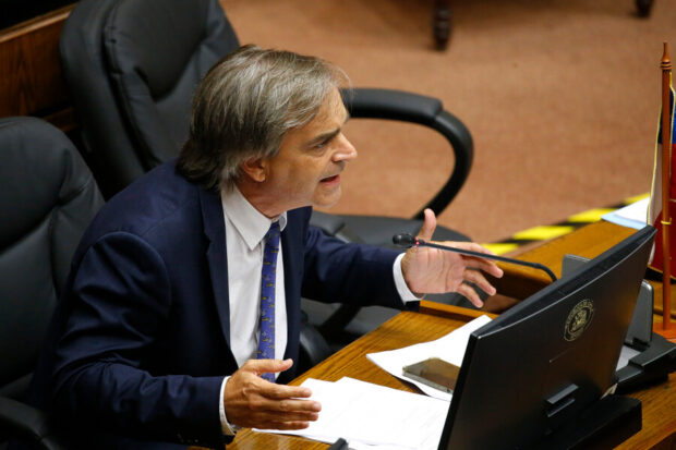Luciano Cruz-Coke durante una intervención en el Senado. El parlamentario esta sentado en un escritorio lleno de papeles mientras habla.