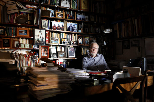 Manuel Antonio Garretón en un escritorio, detrás una biblioteca llena de libros.