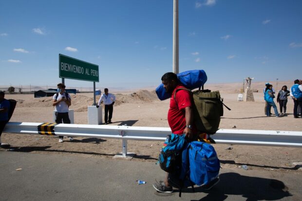 Hombre camina cargando tres bolsos grandes en un carretera. Al fondo se ve un desierto.