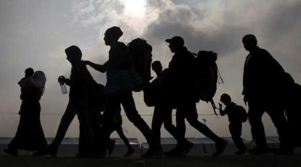 Imagen a contraluz. En la foto se ve la sombra de unas siete personas caminando con grandes bolsos en sus espaldas.
