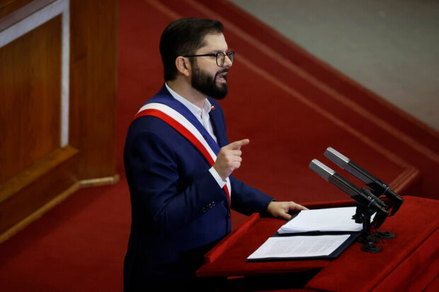 Presidente Boric da un discurso desde un podio, usando la bandera presidencial con los colores azul, blanco y rojo de la bandera de Chile.