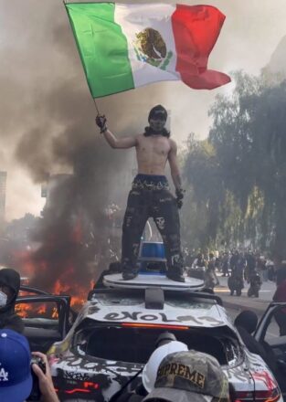 Protestante arriba de un auto siniestrado portando una bandera Mexicana