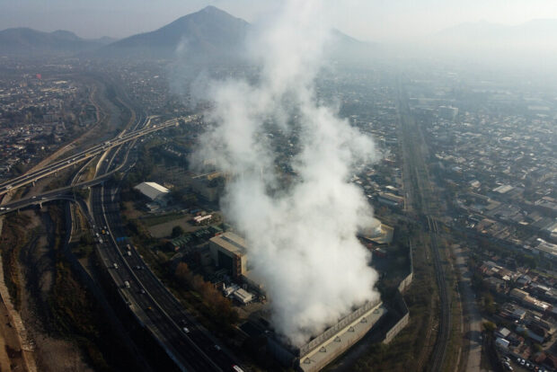Vista desde los cielo de Santiago hacia una empresa termoelectrica, de ella de desprende una gran nube de humo blanca.