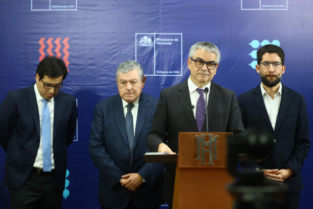 El Ministro de Hacienda, Mario Marcel, en un podio con micrófono, flanqueado por otros tres hombres, en un evento del Ministerio de Hacienda de Chile.