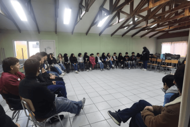 Grupo de niños y jóvenes sentados en círculo en un salón, en el marco de las clases de los campamentos musicales de la FOJI