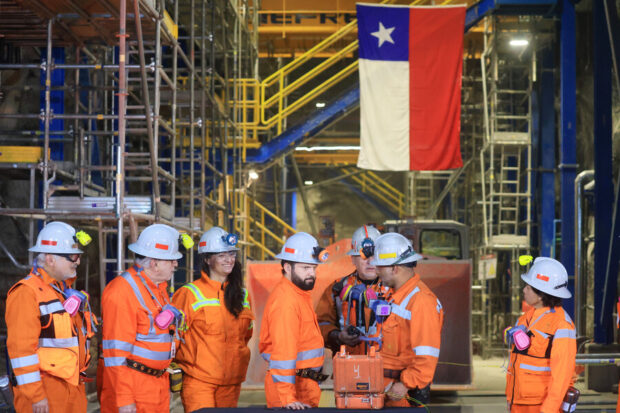 Boric junto a trabajadores de Codelco vestidos de overol naranja y casco de seguridad.