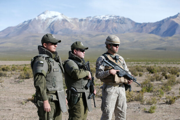 Tres militares al aire libre, detrás de ellos se ve un paisaje montañoso.