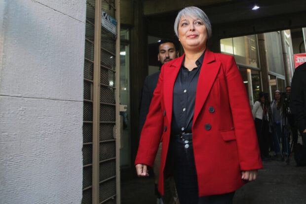 Jeannette Jara, candidata presidencial, vestida con un blazer rojo y una camisa oscura, camina con un rostro decidido en un espacio público