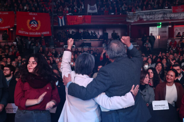 Jara y Carmona de espaldas, frente a ellos cientos de militantes comunistas y banderas del partido en un coliseo (Teatro Caupolicán).
