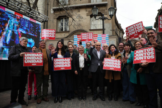 La candidata, Jeannette Jara, está en el centro de la imagen rodeada por su equipo, todos sosteniendo carteles con consignas de su campaña.