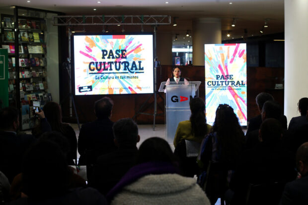 Carolina Arredondo se dirige al publico desde un podio, atrás de ella una pantalla colorida que en el centro dice "Pase Cultural".