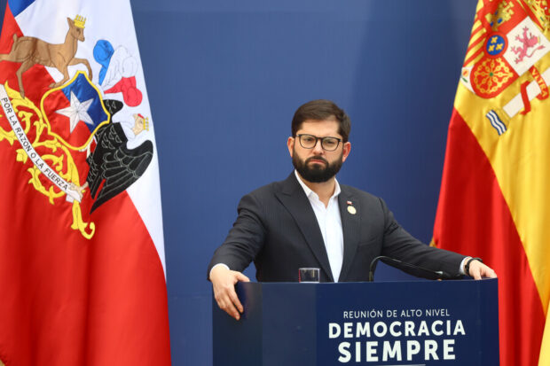 Presidente Gabriel Boric desde un podio, detrás de él se ven la bandera de Chile y la de España.