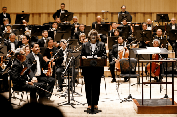 La rectora de la U. de Chile, Rosa Devés, de pie en el centro de la Gran Sala Sinfónica Nacional durante la función inaugural.