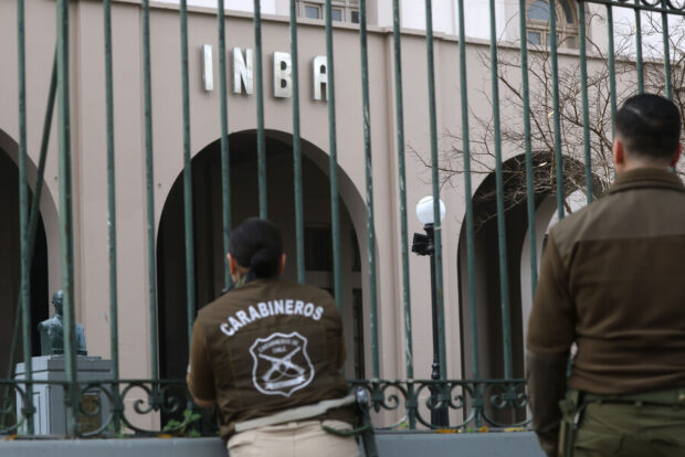 Dos carabineros fotografiados de espalda frente al Internado Nacional Barros Arana (INBA).