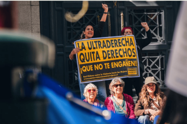 Personas en protesta feminista sostienen un cartel amarillo que dice “La ultraderecha quita derechos. ¡Que no te engañen!” en el centro de Santiago.