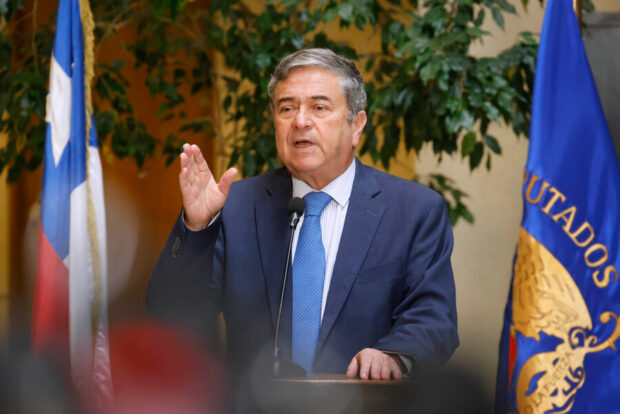 Juan Antonio Coloma, senador chileno, hablando en un podio con la bandera de Chile y el estandarte del Senado de Chile de fondo.