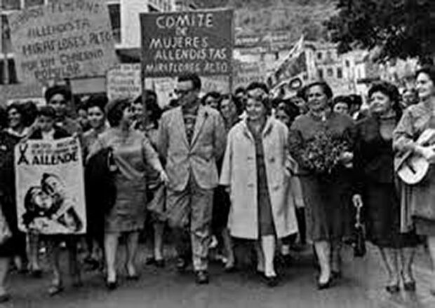 Imagen en blanco y negro de Salvador Allende caminando en la calle con un grupo de mujeres del Comité de Mujeres Allendistas.